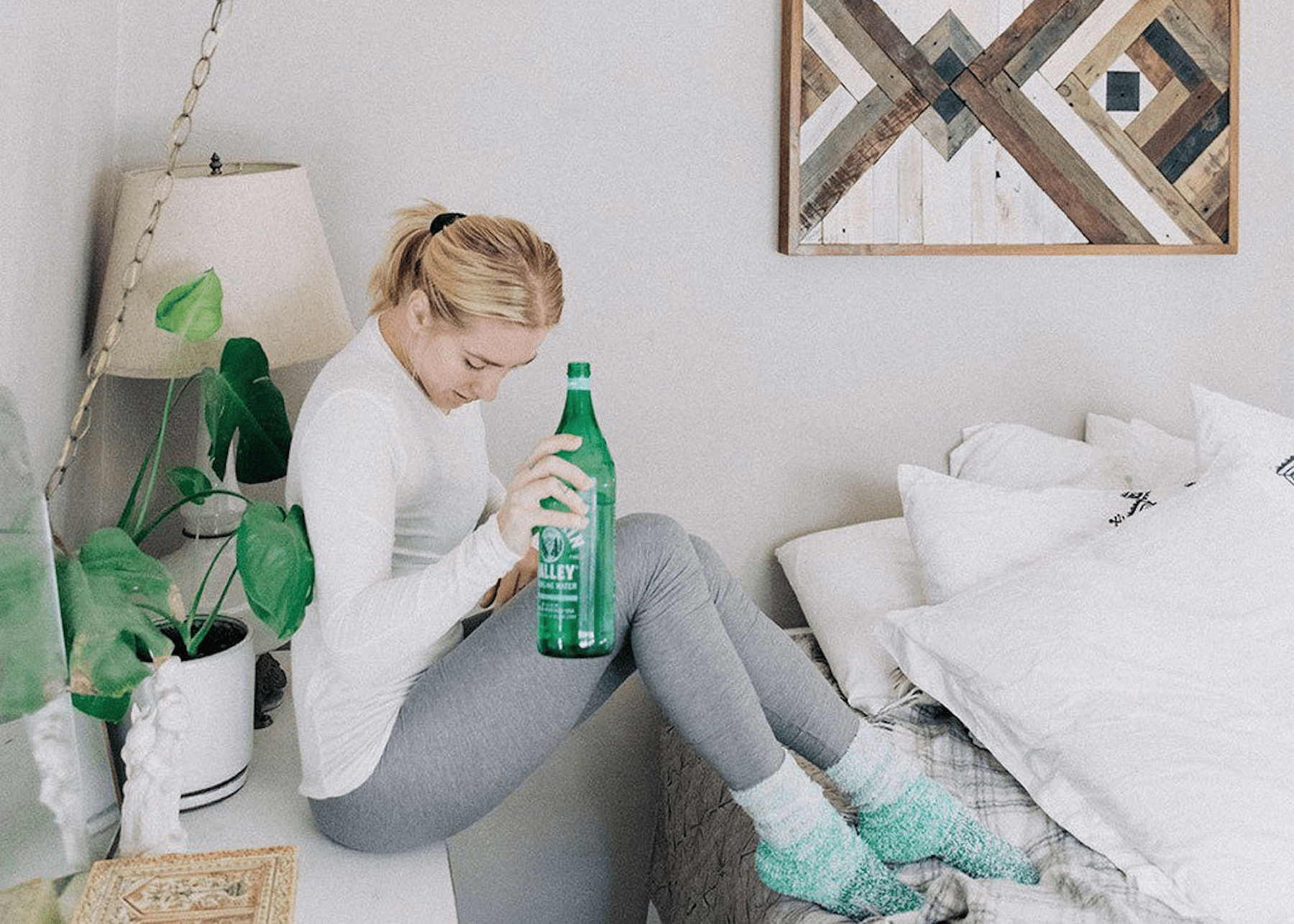 woman sitting on her nightstand with a glass water bottle