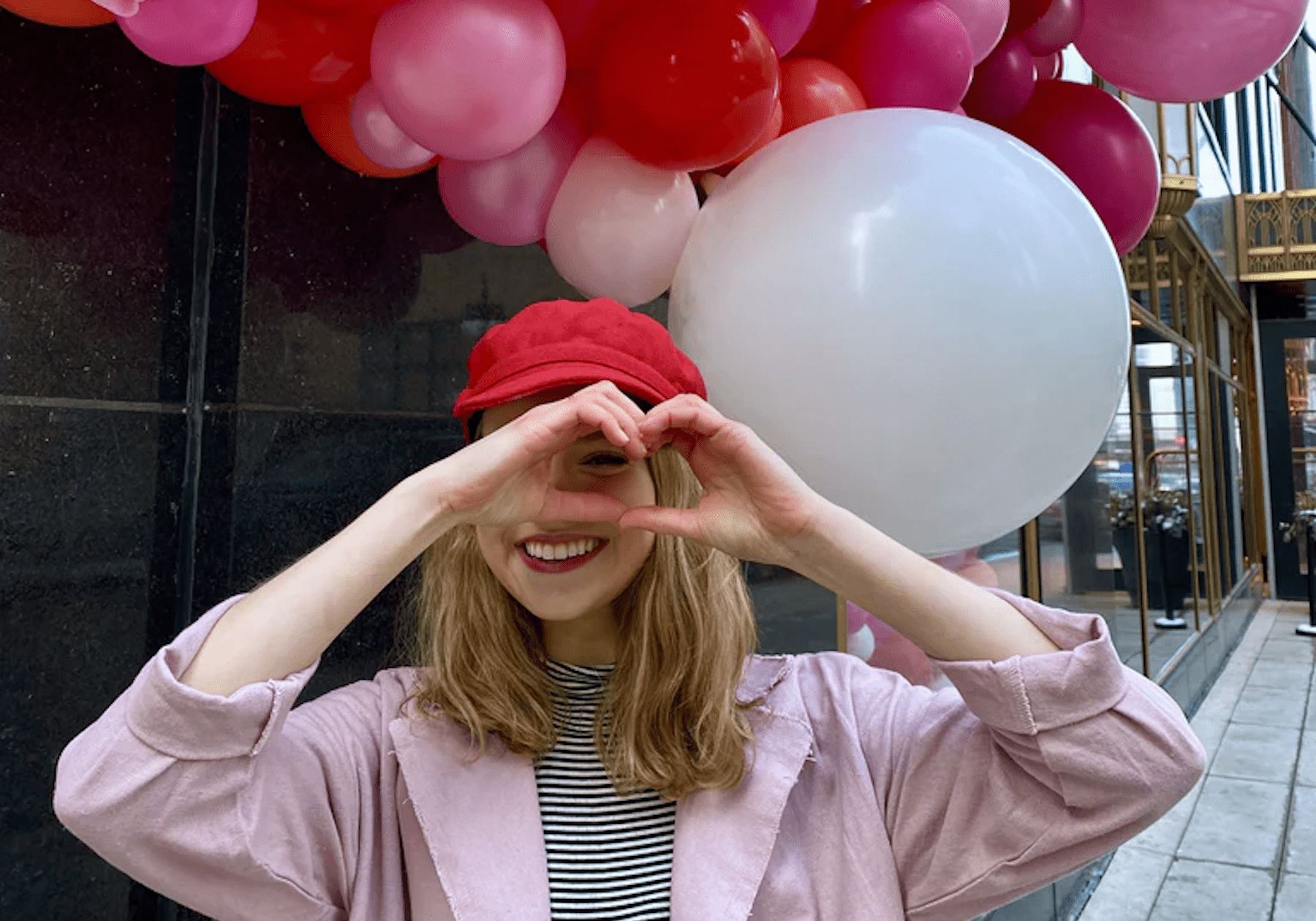 girl holding up heart with her hands in front of red and pink balloons