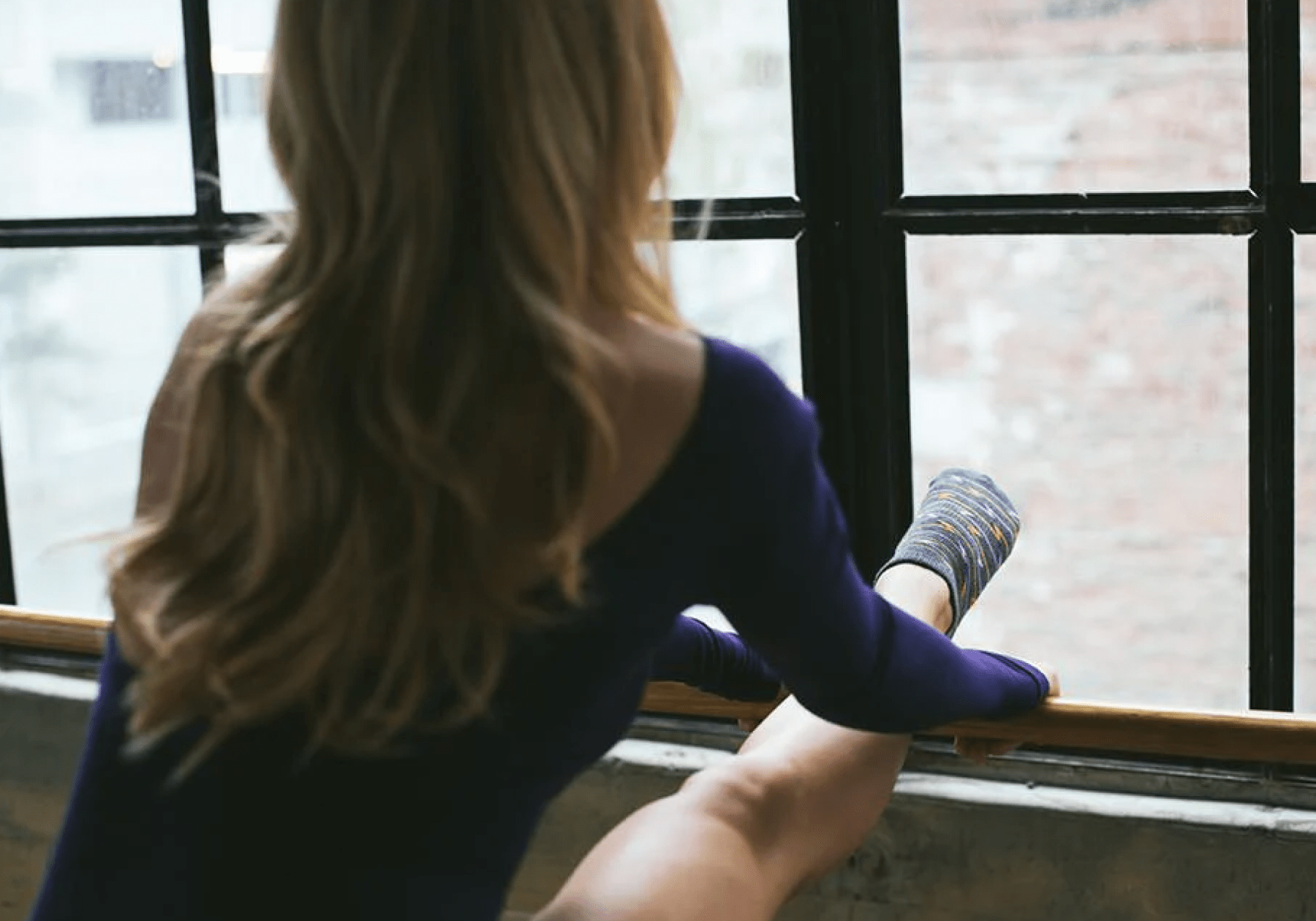 woman stretching leg while looking out the window