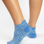Woman wearing a light blue full foot grip sock with white squiggly lines, made for pilates, barre, yoga, and beyond.  