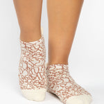 Woman wearing a tan full foot grip sock with brown squiggly lines, made for pilates, barre, yoga, and beyond.  