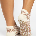 Woman wearing a tan full foot grip sock with brown squiggly lines, made for pilates, barre, yoga, and beyond.  
