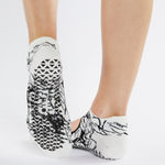 Womean wearing a white strap grip socks with black squiguilly lines. Made for pilates, barre, yoga, and beyond. 