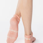 Woman wearing a light pink strap grip sock with white dyed stripes, made for pilates, barre, yoga, and beyond. 