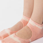 Woman wearing a light pink strap grip sock with white dyed stripes, made for pilates, barre, yoga, and beyond. 