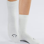 Women wearing white fuzzy plush crew grip socks with a black happy face for recovery and relaxing.  