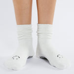 Women wearing white fuzzy plush crew grip socks with a black happy face for recovery and relaxing.  