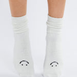Women wearing white fuzzy plush crew grip socks with a black happy face for recovery and relaxing.  