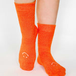 Women wearing orange fuzzy plush crew grip socks with a white happy face for recovery and relaxing.  