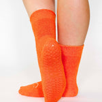 Women wearing orange fuzzy plush crew grip socks with a white happy face for recovery and relaxing.  
