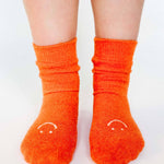 Women wearing orange fuzzy plush crew grip socks with a white happy face for recovery and relaxing.  