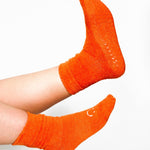 Women wearing orange fuzzy plush crew grip socks with a white happy face for recovery and relaxing.  
