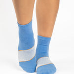 Woman wearing a blue ankle grip sock with a solid light blue stripe in the center, made for pilates, barre, yoga, and beyond.  
