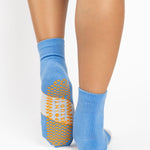 Woman wearing a blue ankle grip sock with a solid light blue stripe in the center, made for pilates, barre, yoga, and beyond.  