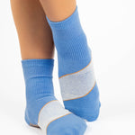 Woman wearing a blue ankle grip sock with a solid light blue stripe in the center, made for pilates, barre, yoga, and beyond.  