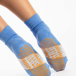 Woman wearing a blue ankle grip sock with a solid light blue stripe in the center, made for pilates, barre, yoga, and beyond.  