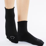 Women wearing black ankle grip socks with white happy face for Pilates, Barre, Yoga, and beyond. 
