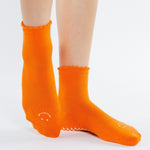 Women wearing orange ankle grip socks with white happy face for Pilates, Barre, Yoga, and beyond. 