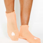 Women wearing a light apricot orange full foot grip sock with a white heart motif on the top made for Pilates, Barre, Yoga, and beyond. 
