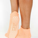 Women wearing a light apricot orange full foot grip sock with a white heart motif on the top made for Pilates, Barre, Yoga, and beyond. 
