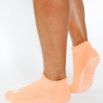 Women wearing a light apricot orange full foot grip sock with a white heart motif on the top made for Pilates, Barre, Yoga, and beyond. 