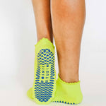 Women wearing a lime full foot grip sock with a blue heart motif on the top made for Pilates, Barre, Yoga, and beyond. 