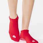 Women wearing a red full foot grip sock with a pink heart motif on the top made for Pilates, Barre, Yoga, and beyond. 