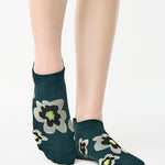 Women wearing a green full foot grip sock with big flowers all around made for pilates, yoga, barre, and beyond.