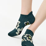 Women wearing a green full foot grip sock with big flowers all around made for pilates, yoga, barre, and beyond.
