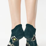 Women wearing a green full foot grip sock with big flowers all around made for pilates, yoga, barre, and beyond.
