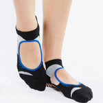 Womean wearing black strap grip socks with colorful blue and grey features. Made for pilates, barre, yoga, and beyond. 