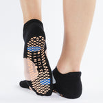 Womean wearing black strap grip socks with colorful blue and grey features. Made for pilates, barre, yoga, and beyond. 