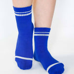 Women wearing a bright blue grip sock with white stripes on the toes and top ankle cuff made for Pilates, Barre, Yoga, and beyond. 
