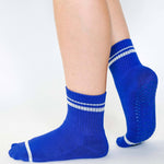 Women wearing a bright blue grip sock with white stripes on the toes and top ankle cuff made for Pilates, Barre, Yoga, and beyond. 