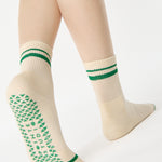 Women wearing a beige ankle grip sock with green stripes on the toes and top ankle cuff made for Pilates, Barre, Yoga, and beyond. 
