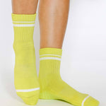 Women wearing a lime yellow grip sock with white stripes on the toes and top ankle cuff made for Pilates, Barre, Yoga, and beyond. 