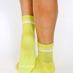 Women wearing a lime yellow grip sock with white stripes on the toes and top ankle cuff made for Pilates, Barre, Yoga, and beyond. 