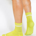 Women wearing a lime yellow grip sock with white stripes on the toes and top ankle cuff made for Pilates, Barre, Yoga, and beyond. 