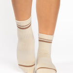 Women wearing a solid nougat white ankle grip sock with brown stripes on the toes and top ankle cuff made for Pilates, Barre, Yoga, and beyond. 