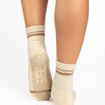 Women wearing a solid nougat white ankle grip sock with brown stripes on the toes and top ankle cuff made for Pilates, Barre, Yoga, and beyond. 