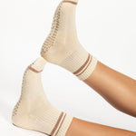 Women wearing a solid nougat white ankle grip sock with brown stripes on the toes and top ankle cuff made for Pilates, Barre, Yoga, and beyond. 