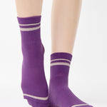 Women wearing a purple ankle grip sock with off white stripes on the toes and top ankle cuff made for Pilates, Barre, Yoga, and beyond. 