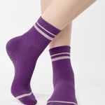 Women wearing a purple ankle grip sock with off white stripes on the toes and top ankle cuff made for Pilates, Barre, Yoga, and beyond. 
