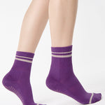 Women wearing a purple ankle grip sock with off white stripes on the toes and top ankle cuff made for Pilates, Barre, Yoga, and beyond. 