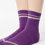Women wearing a purple ankle grip sock with off white stripes on the toes and top ankle cuff made for Pilates, Barre, Yoga, and beyond. 