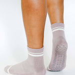 Women wearing a solid light purple ankle grip sock with white stripes on the toes and top ankle cuff made for Pilates, Barre, Yoga, and beyond. 