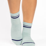 Women wearing a light sky blue ankle grip sock with navy blue stripes on the toes and top ankle cuff made for Pilates, Barre, Yoga, and beyond. 