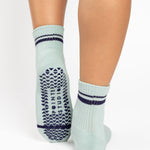 Women wearing a light sky blue ankle grip sock with navy blue stripes on the toes and top ankle cuff made for Pilates, Barre, Yoga, and beyond. 