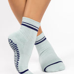 Women wearing a light sky blue ankle grip sock with navy blue stripes on the toes and top ankle cuff made for Pilates, Barre, Yoga, and beyond. 