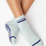 Women wearing a light sky blue ankle grip sock with navy blue stripes on the toes and top ankle cuff made for Pilates, Barre, Yoga, and beyond. 